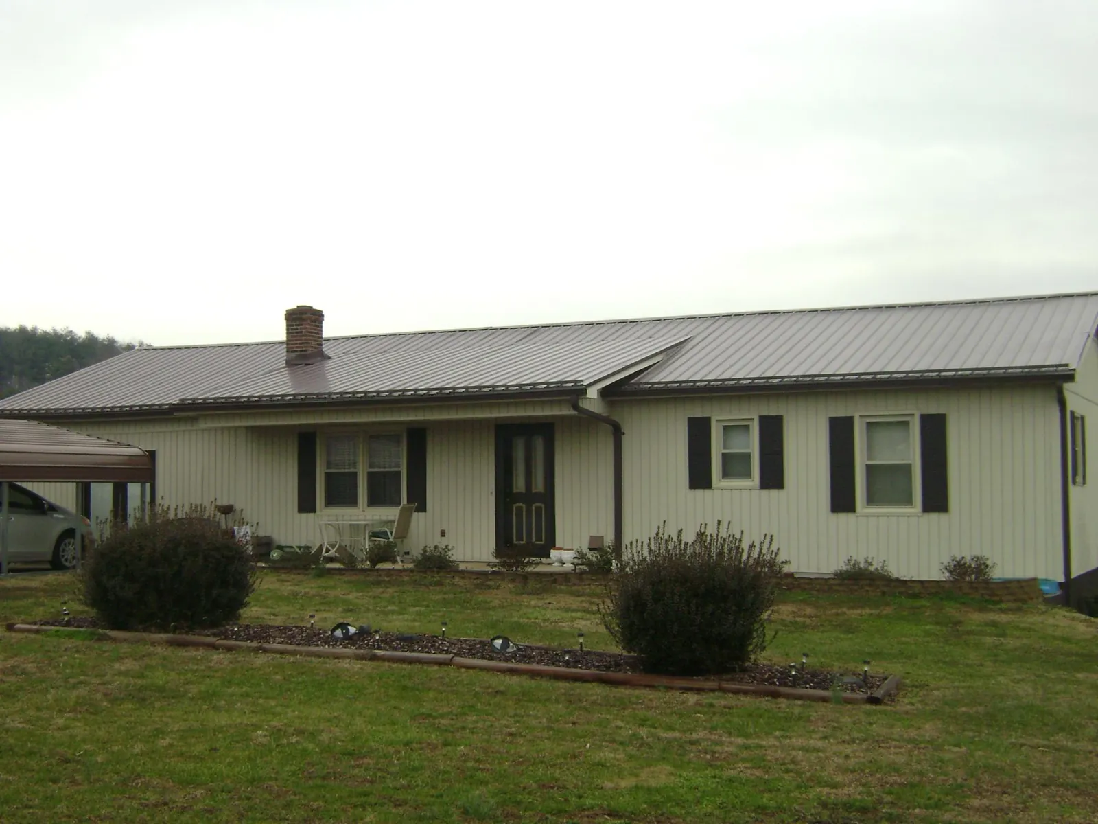 Brown metal roof on a cream sided ranch home with a brick chimney in Arlington